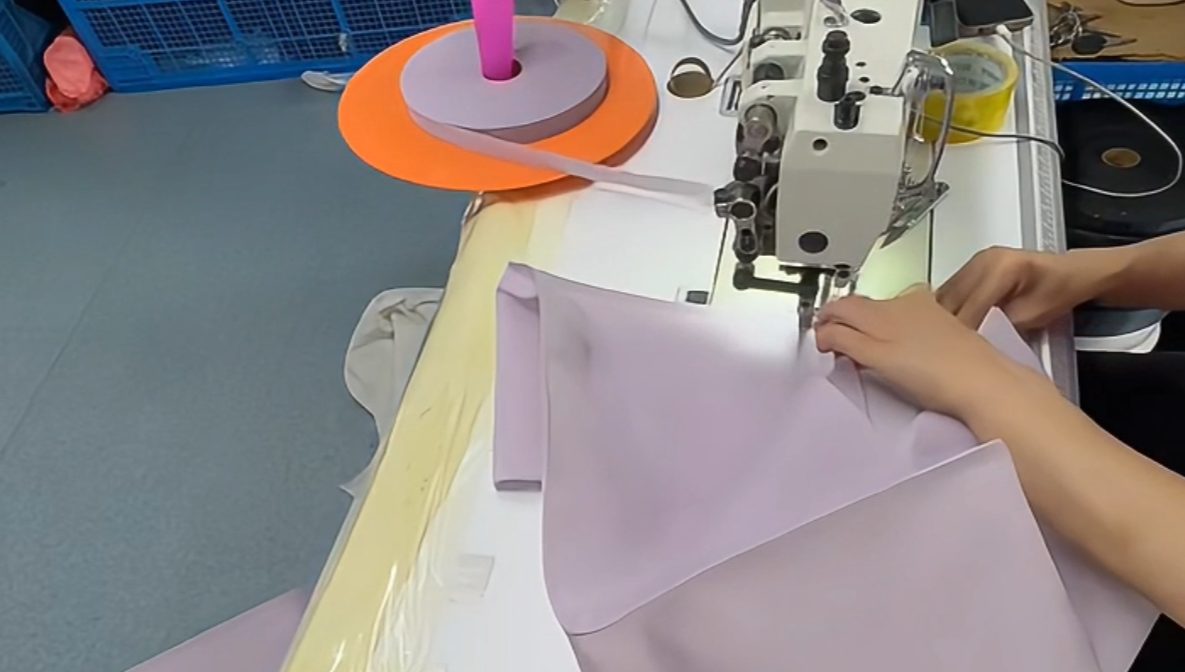 Sewing workshop — operator running binding tape along a finished fabric edge on an industrial machine
